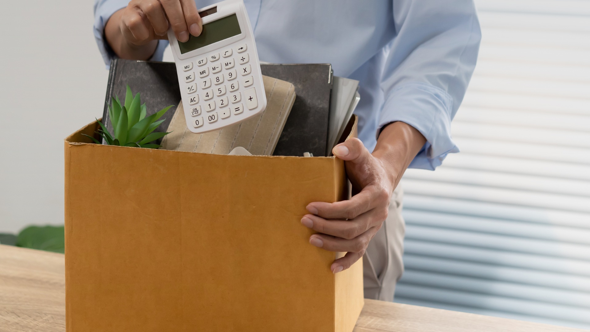 Persona empacando objetos personales de oficina en una caja tras un despido laboral
